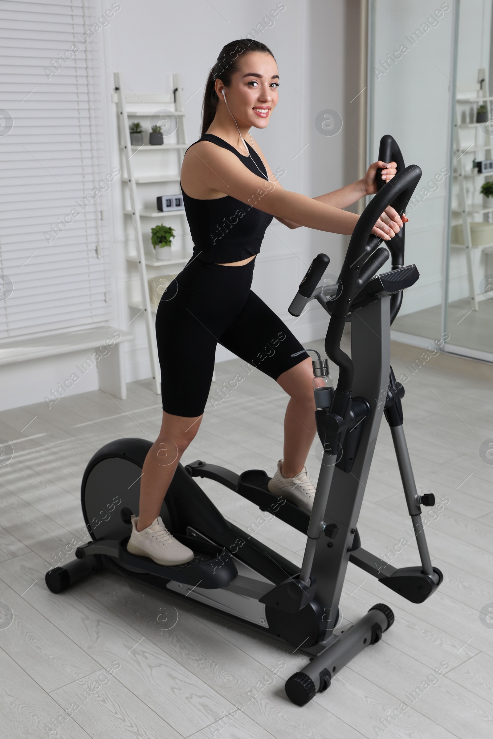 Photo of Happy young woman training on elliptical machine at home