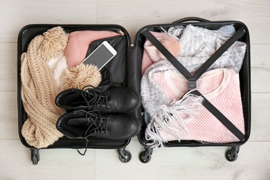 Packed suitcase with warm clothes and smartphone on wooden background, top view. Space for text