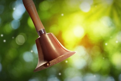 Image of Shiny school bell with wooden handle outdoors. Bokeh effect