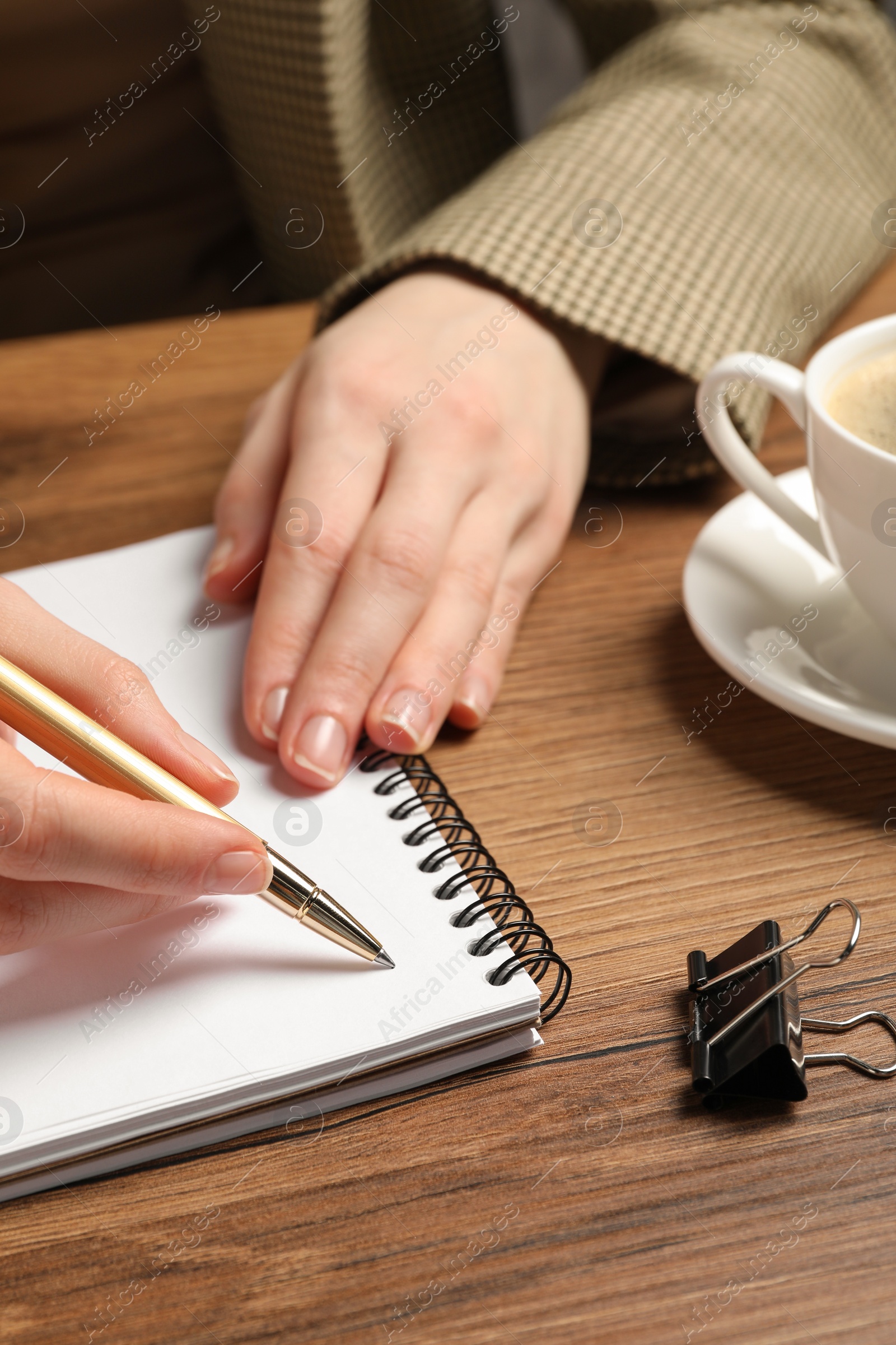 Photo of Woman writing in notebook at wooden table, closeup