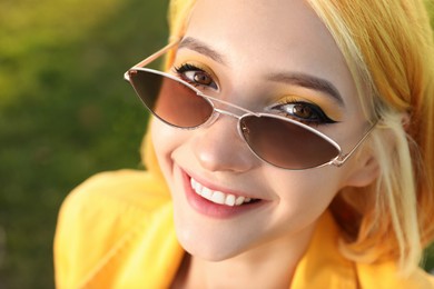 Beautiful young woman with bright dyed hair on blurred green background, closeup