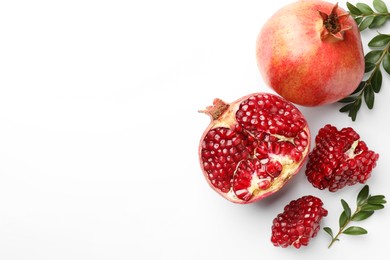 Photo of Fresh pomegranates and green leaves on white background, flat lay. Space for text