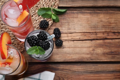 Photo of Different delicious lemonades made with soda water on wooden table, flat lay. Space for text