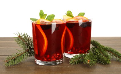 Photo of Aromatic Christmas Sangria drink in glasses and fir branches on wooden table against white background