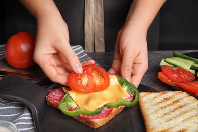 Photo of Woman adding tomato to sandwich at grey table, closeup