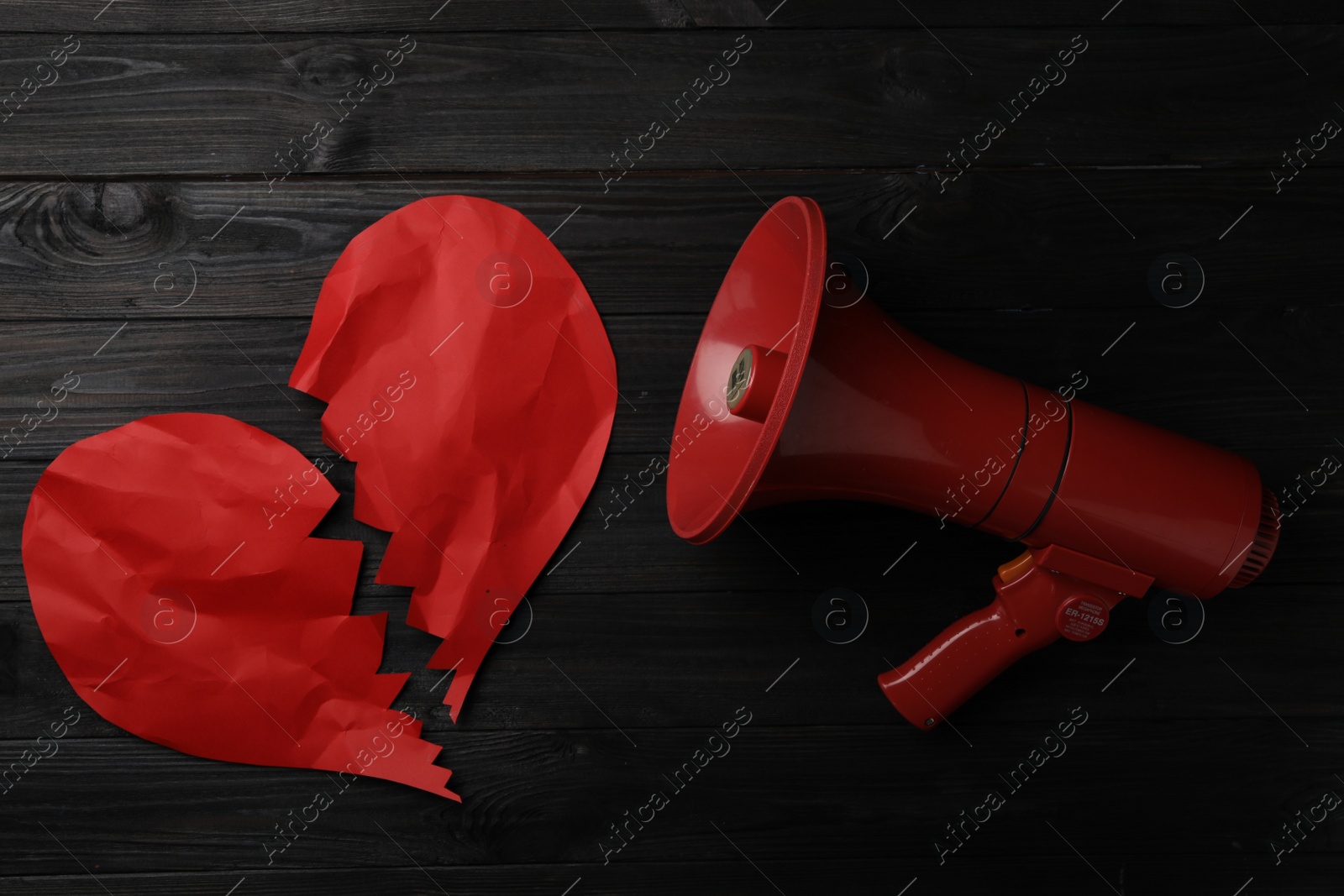 Photo of Torn red paper heart and megaphone on black wooden background, flat lay. Relationship problems concept