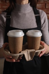 Photo of Barista holding takeaway paper cups with coffee in cafe, closeup