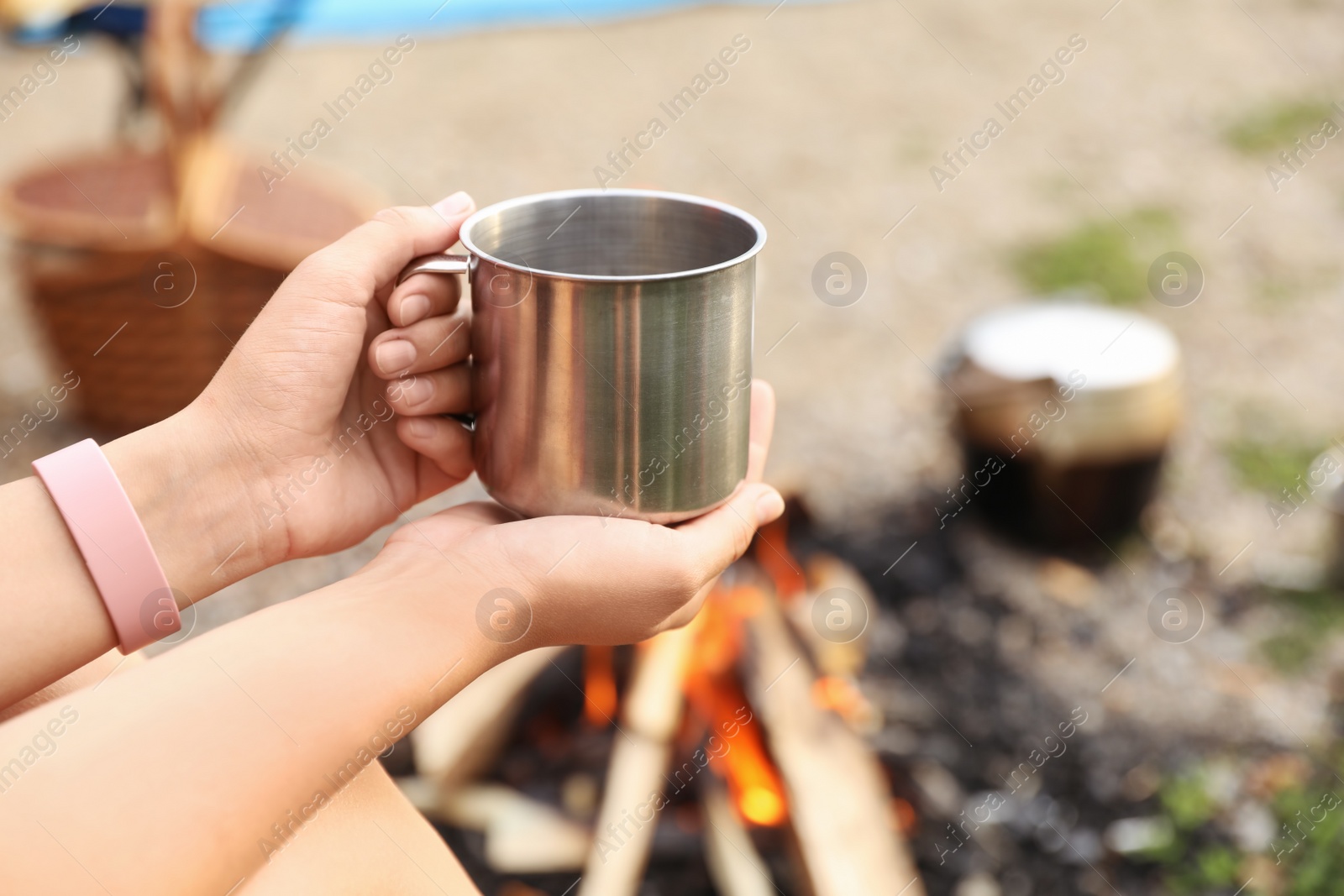 Photo of Young woman with mug near bonfire outdoors, focus on hands. Camping season