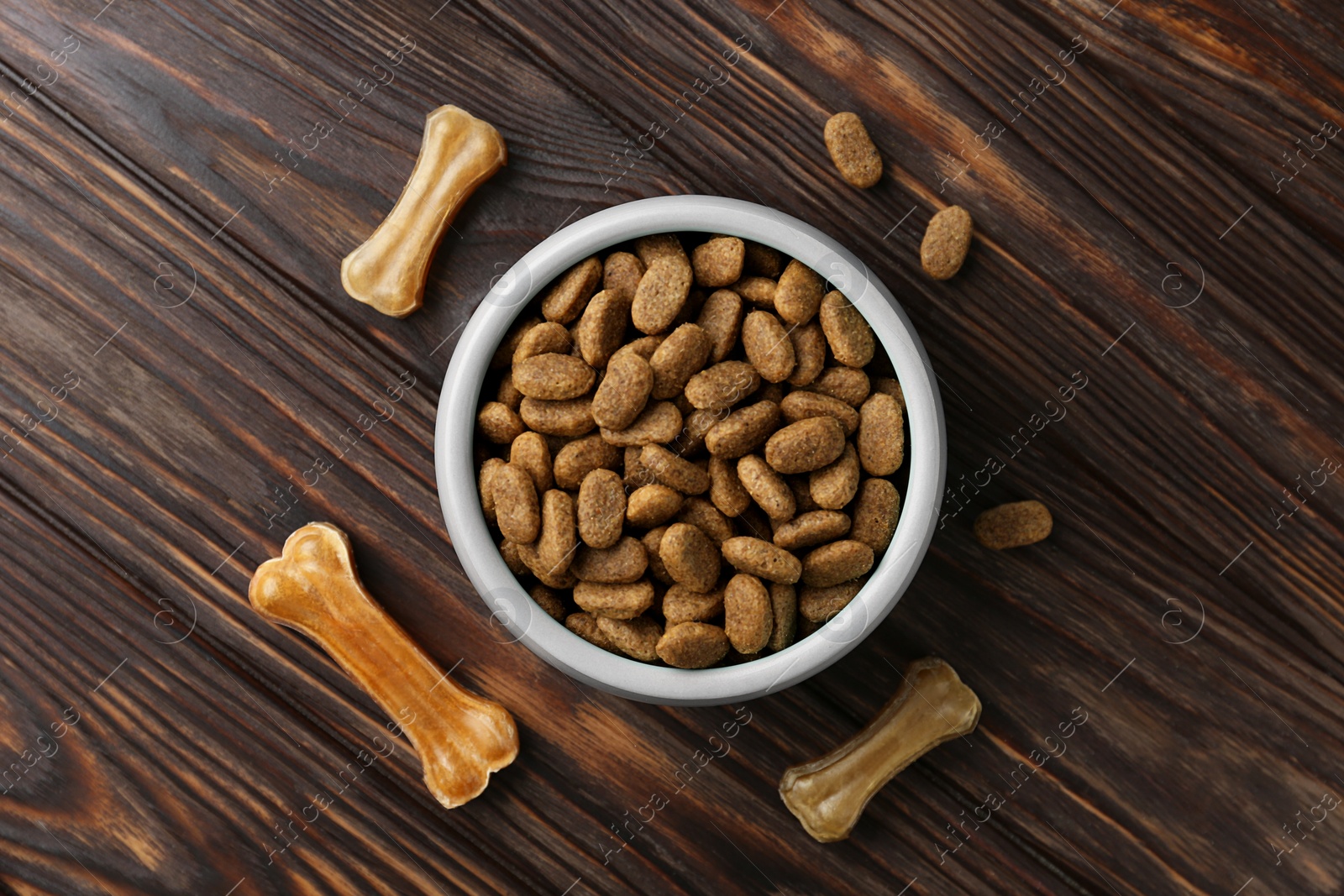 Photo of Dry dog food and treats (chew bones) on wooden floor, flat lay