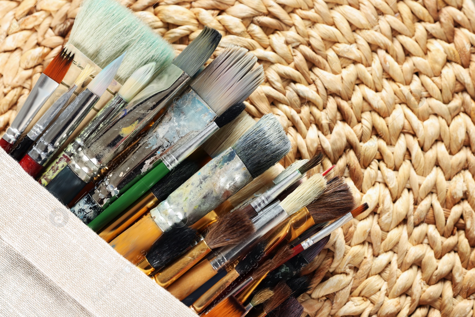 Photo of Many paintbrushes in sack on wicker mat, top view. Space for text