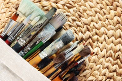 Many paintbrushes in sack on wicker mat, top view. Space for text