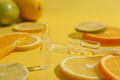 Skincare ampoules with vitamin C and citrus slices on yellow background, closeup