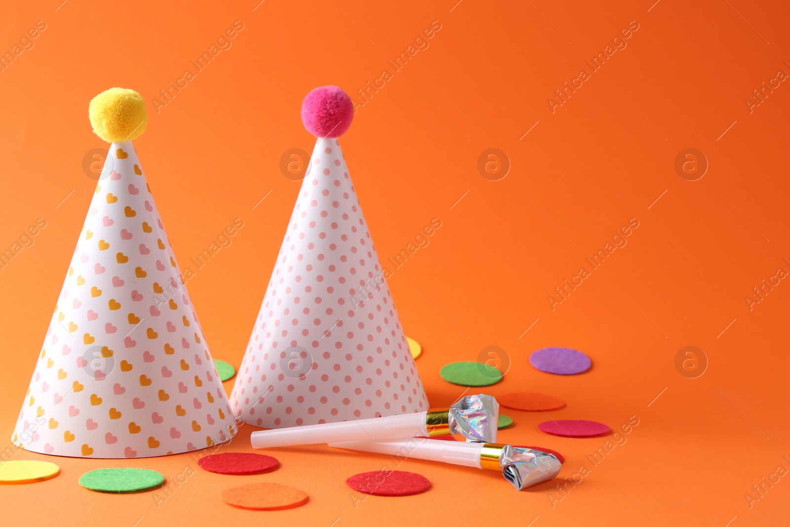 Photo of Party hats and other bright decor elements on orange background, space for text