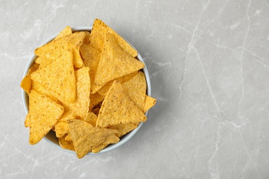 Bowl with tasty Mexican nachos chips on grey table, top view. Space for text