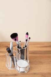 Photo of Organizer with cosmetic products for makeup on table against light wall