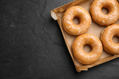 Photo of Delicious donuts on black table, top view. Space for text