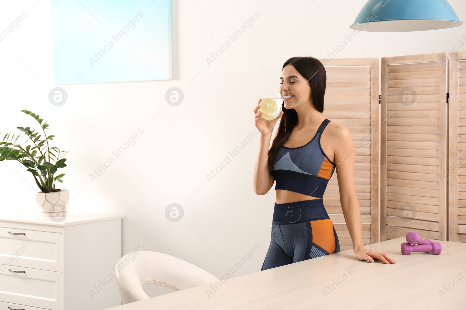 Photo of Beautiful sportive woman drinking fresh lemon water indoors. Space for text