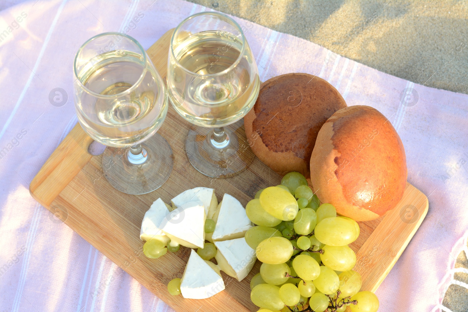 Photo of Glasses with white wine and snacks for beach picnic on sand outdoors, above view