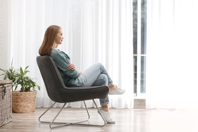 Photo of Young woman sitting in armchair near window at home