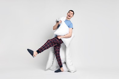 Happy man in pyjama with blanket and pillow on light grey background