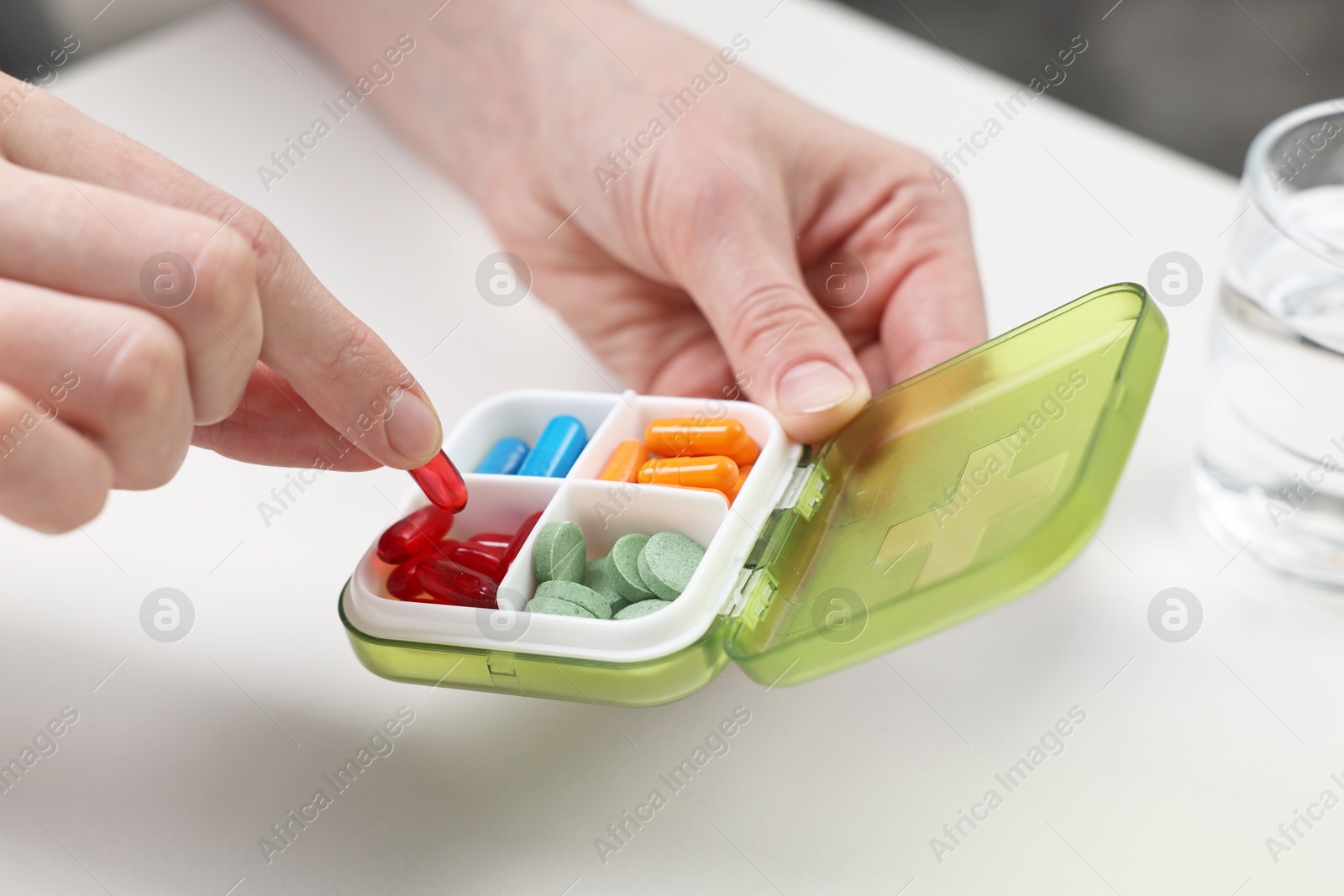 Photo of Woman with pills, organizer and glass of water at white table, closeup