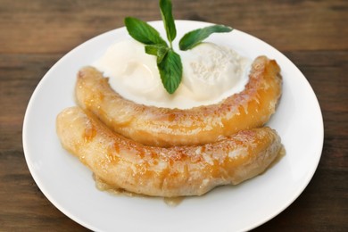 Photo of Plate with delicious fried bananas, ice cream and mint leaves on wooden table, closeup