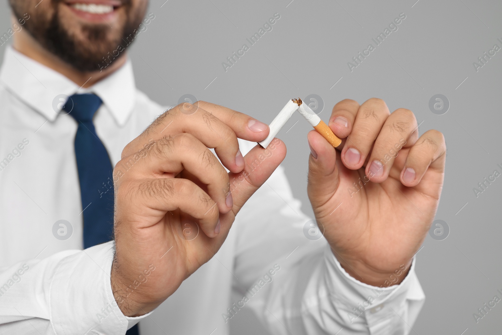 Photo of Stop smoking concept. Man breaking cigarette on light grey background, closeup