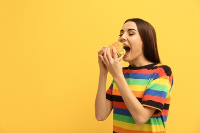 Young woman eating tasty burger on color background. Space for text