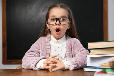 Cute little child wearing glasses at desk in classroom. First time at school