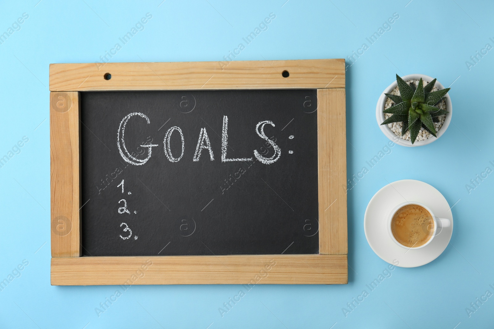 Photo of Small blackboard with empty list of goals, houseplant and cup of coffee on light blue background, flat lay. Space for text