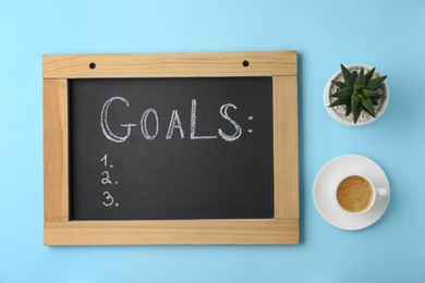 Photo of Small blackboard with empty list of goals, houseplant and cup of coffee on light blue background, flat lay. Space for text