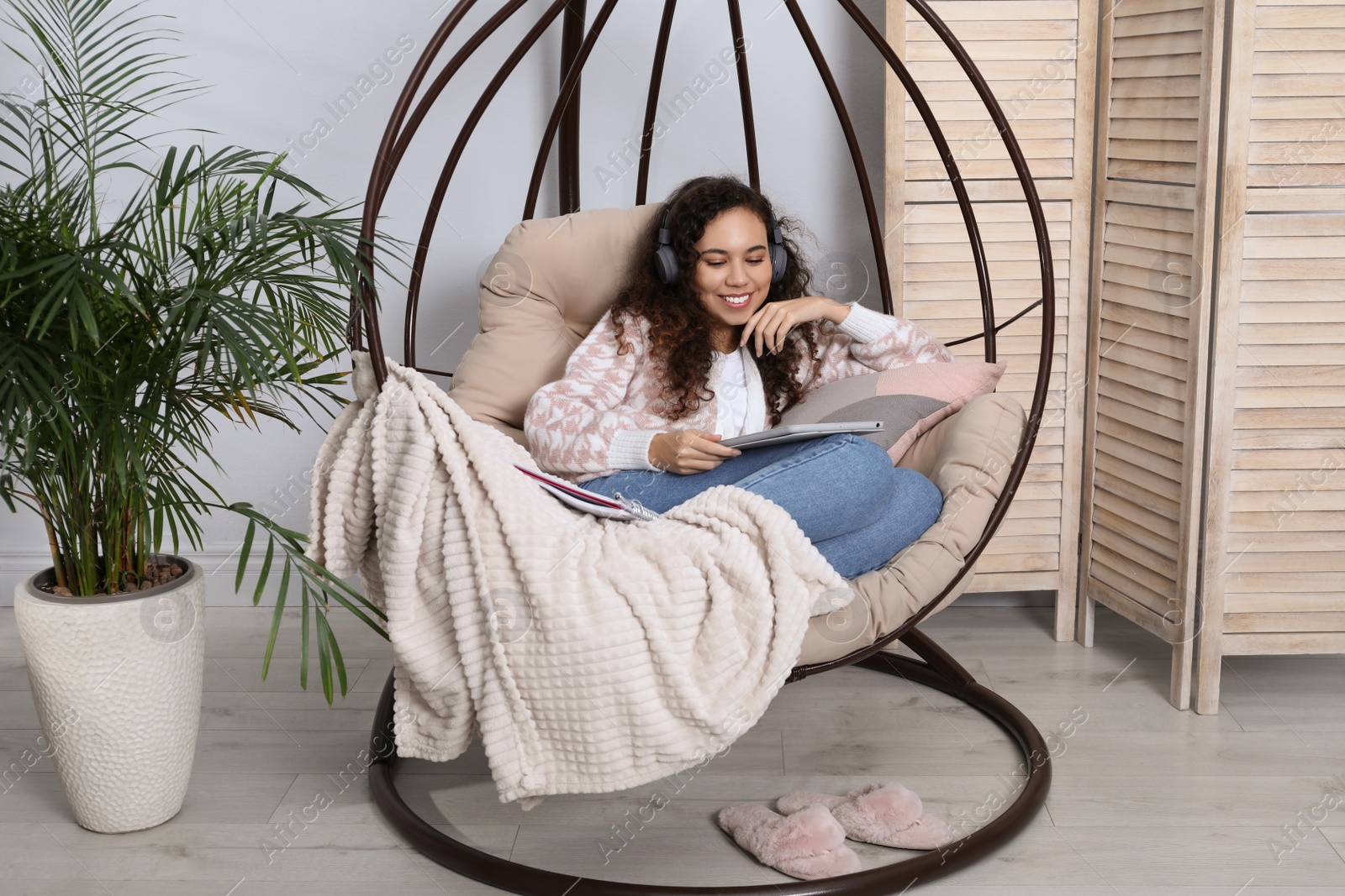 Photo of African American woman with headphones and tablet studying in egg chair at home. Distance learning