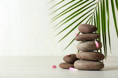 Stack of spa stones, palm leaf and petals on table against white background, space for text