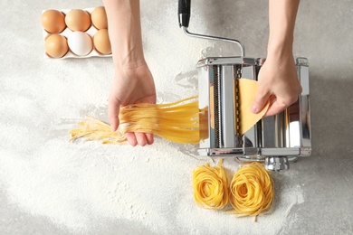 Young woman preparing noodles with pasta maker at table, top view