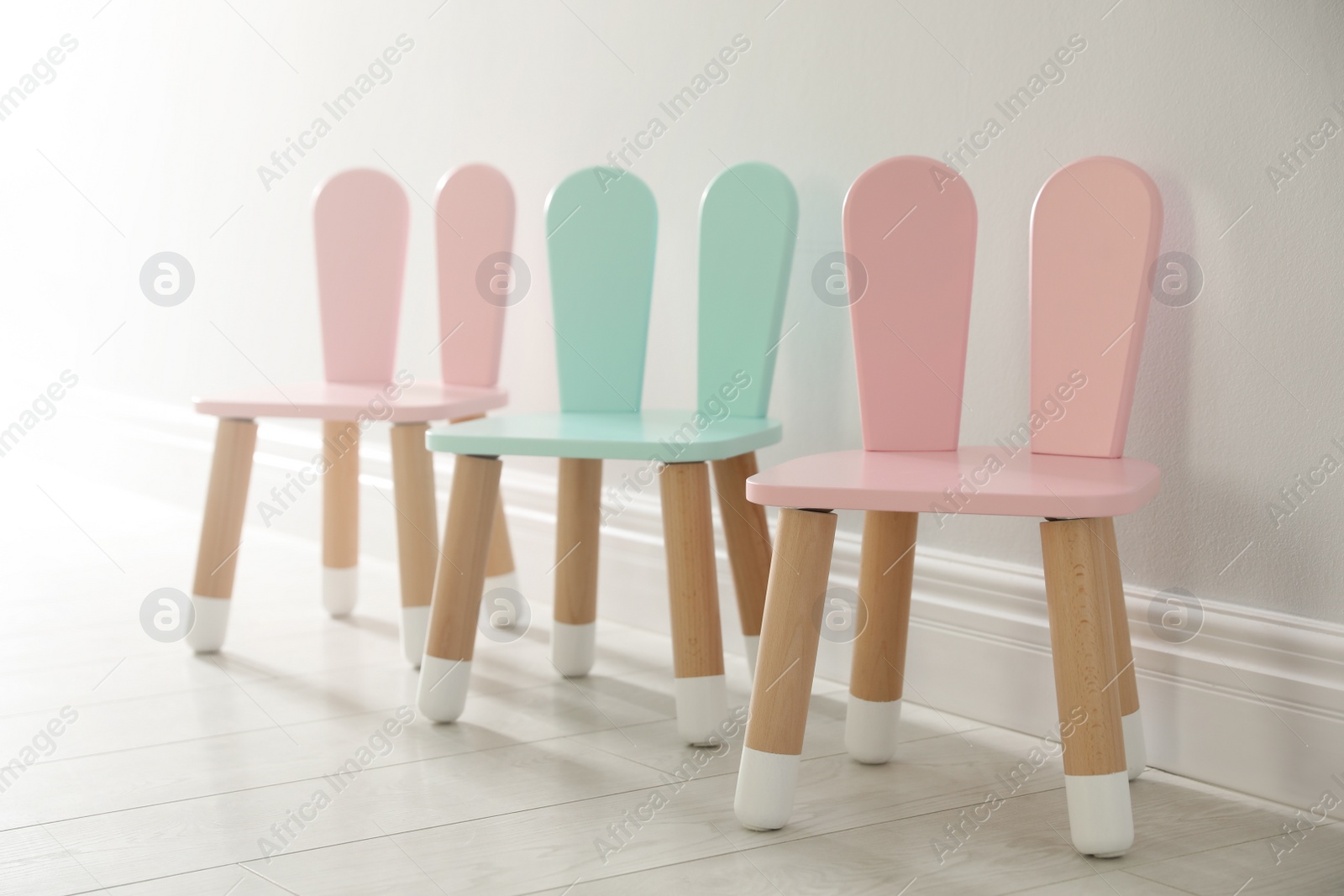 Photo of Cute little chairs with bunny ears near white wall indoors. Children's room interior