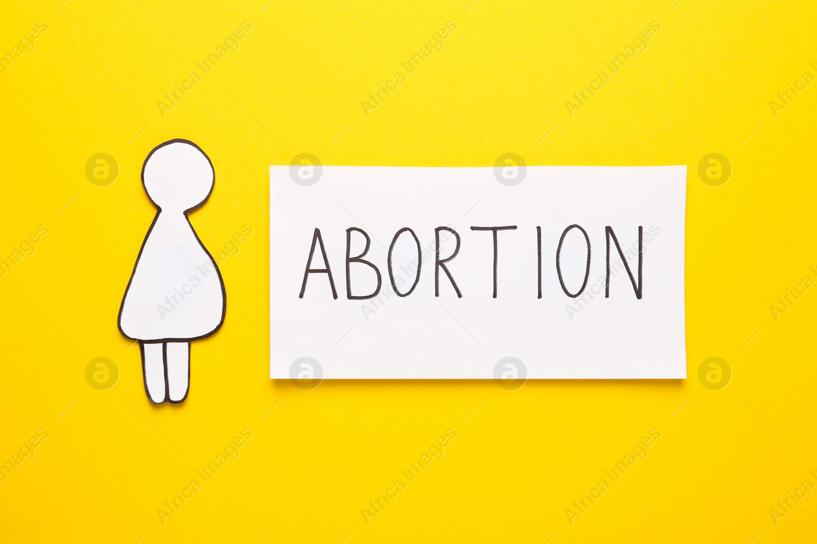 Photo of Note with word Abortion and pregnant woman paper cutout on yellow background, flat lay