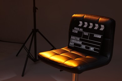 Photo of Casting call. Chair and clapperboard in modern studio, closeup. Space for text