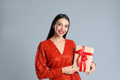 Woman in red dress holding Christmas gift on grey background