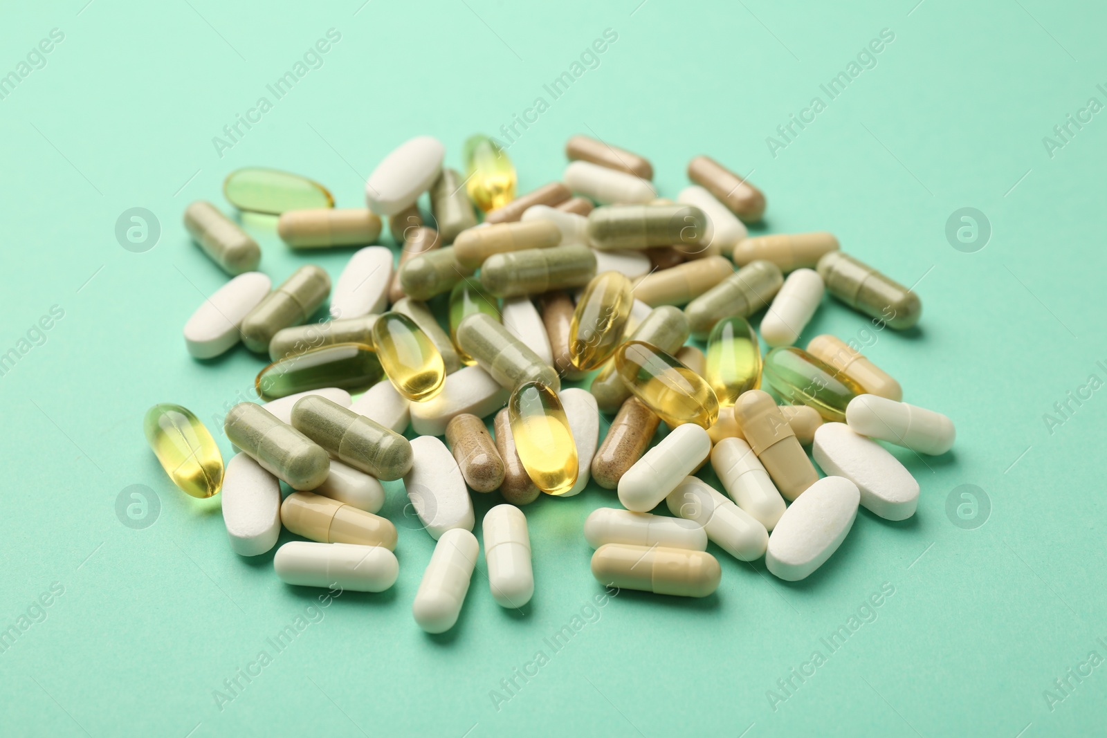 Photo of Different vitamin capsules on turquoise background, closeup