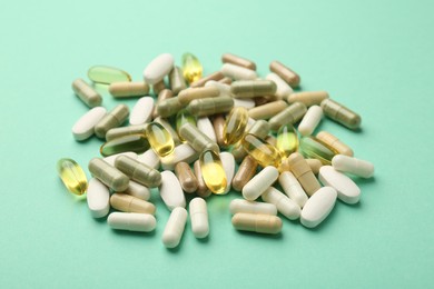 Photo of Different vitamin capsules on turquoise background, closeup