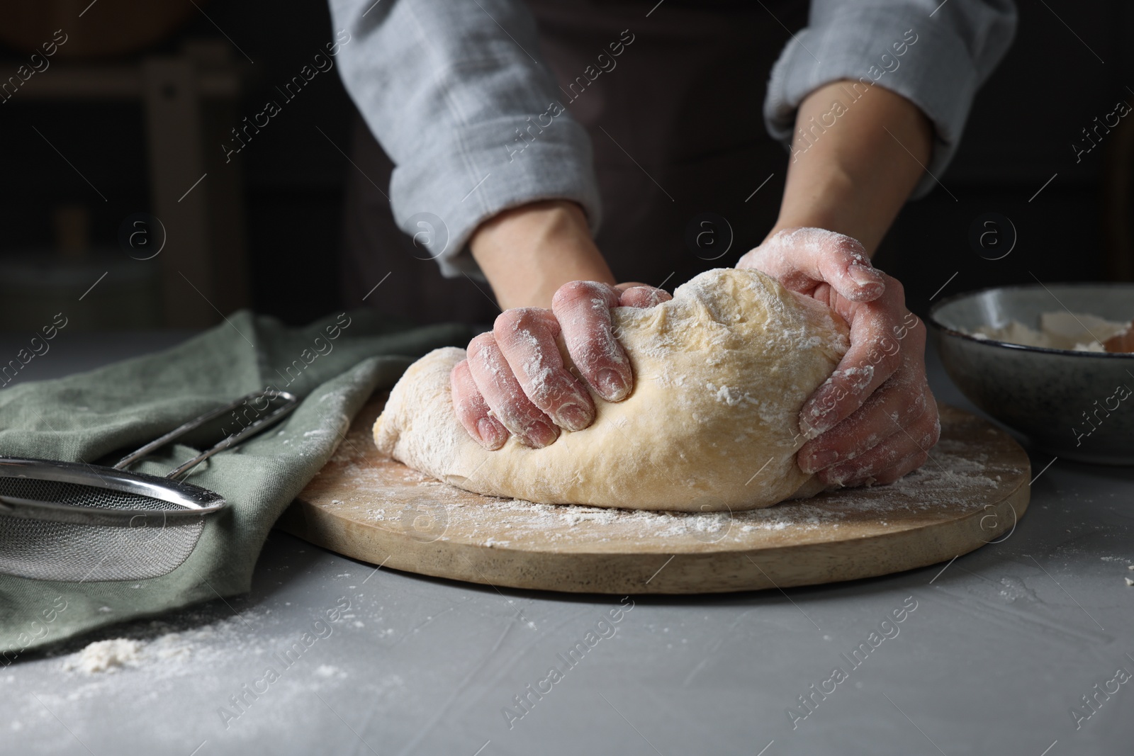 Photo of Woman kneading dough at grey table, closeup