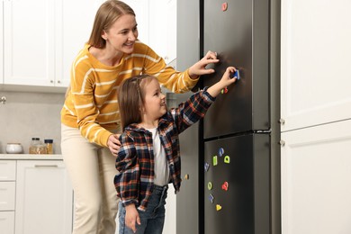 Photo of Mom and daughter putting magnetic letters on fridge at home. Learning alphabet