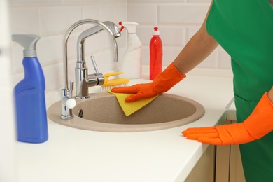 Photo of Woman in protective gloves cleaning kitchen sink with rag, closeup
