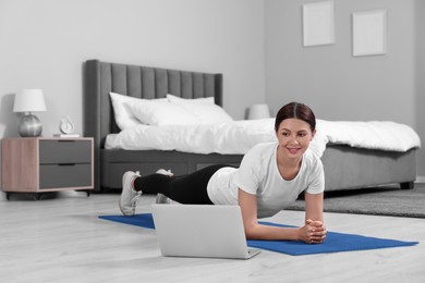 Photo of Happy woman doing plank exercise and watching video tutorial via laptop at home. Space for text