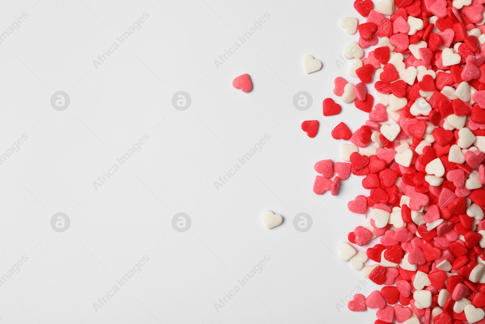 Photo of Bright heart shaped sprinkles on white background, flat lay. Space for text