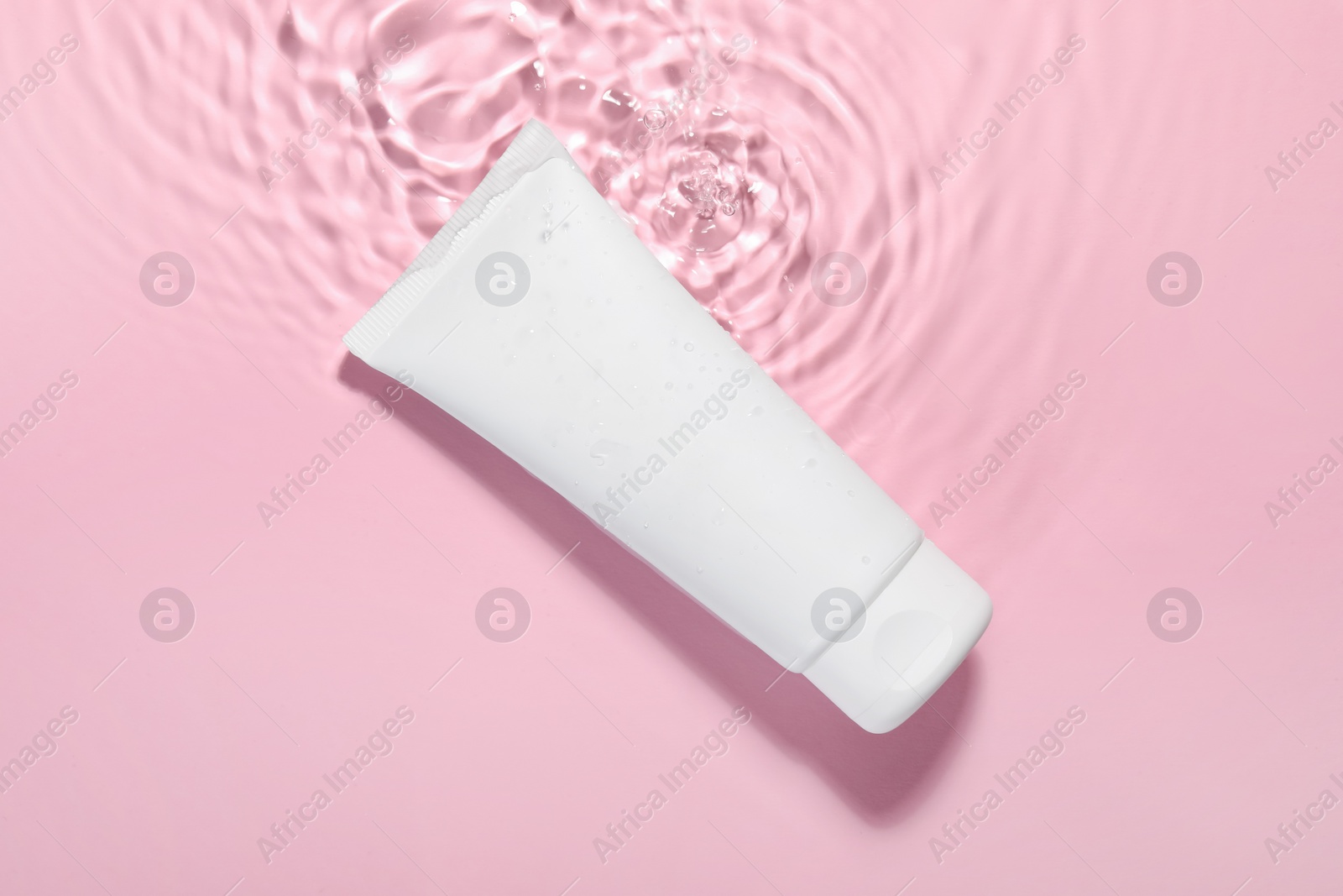 Photo of Tube of facial cleanser in water against pink background, top view