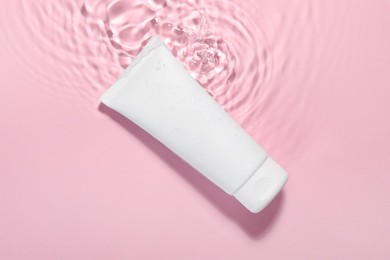 Photo of Tube of facial cleanser in water against pink background, top view