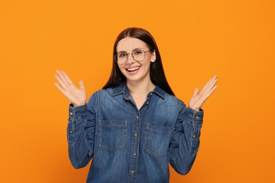 Portrait of emotional woman in stylish eyeglasses on orange background