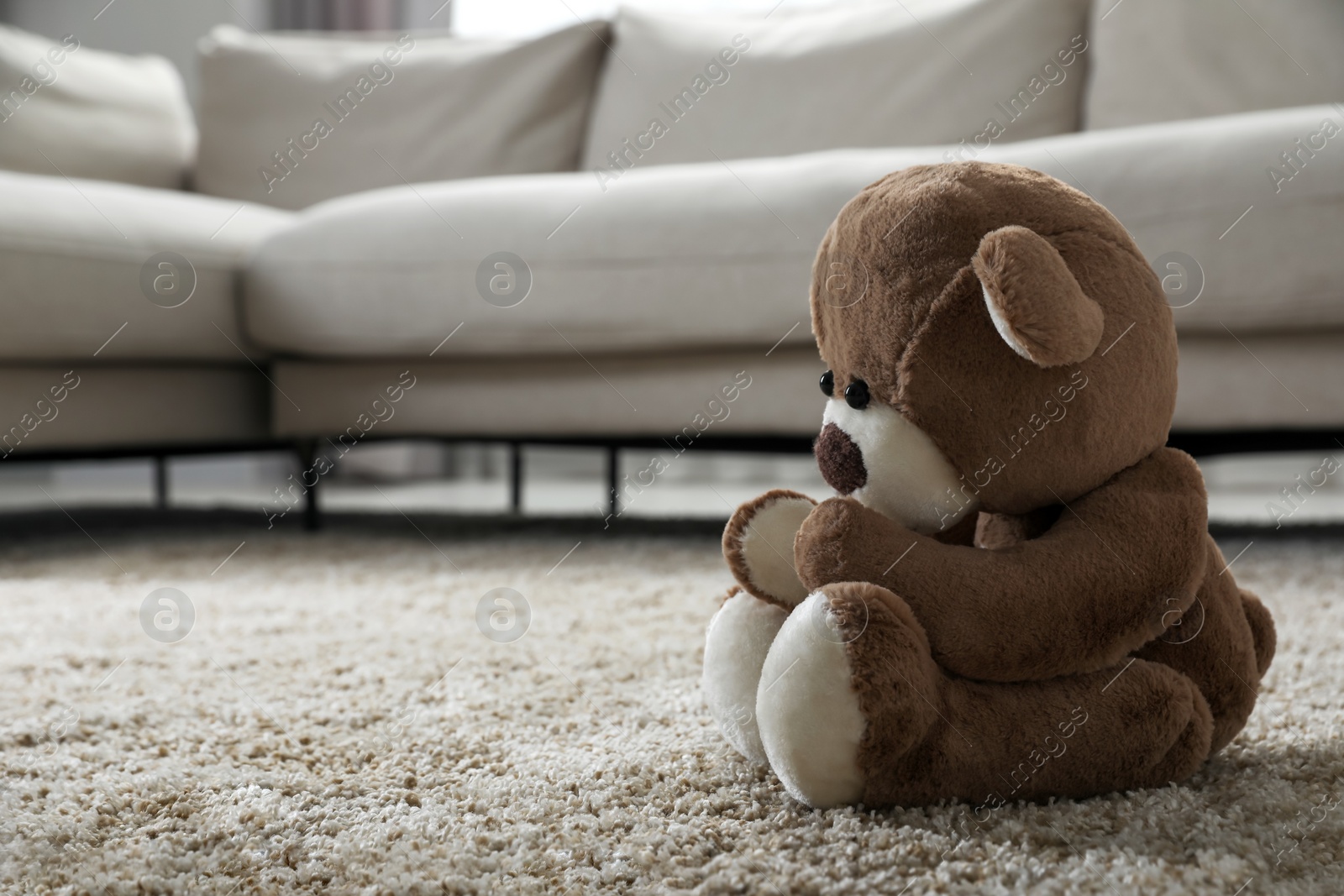 Photo of Cute lonely teddy bear on floor near sofa in room. Space for text
