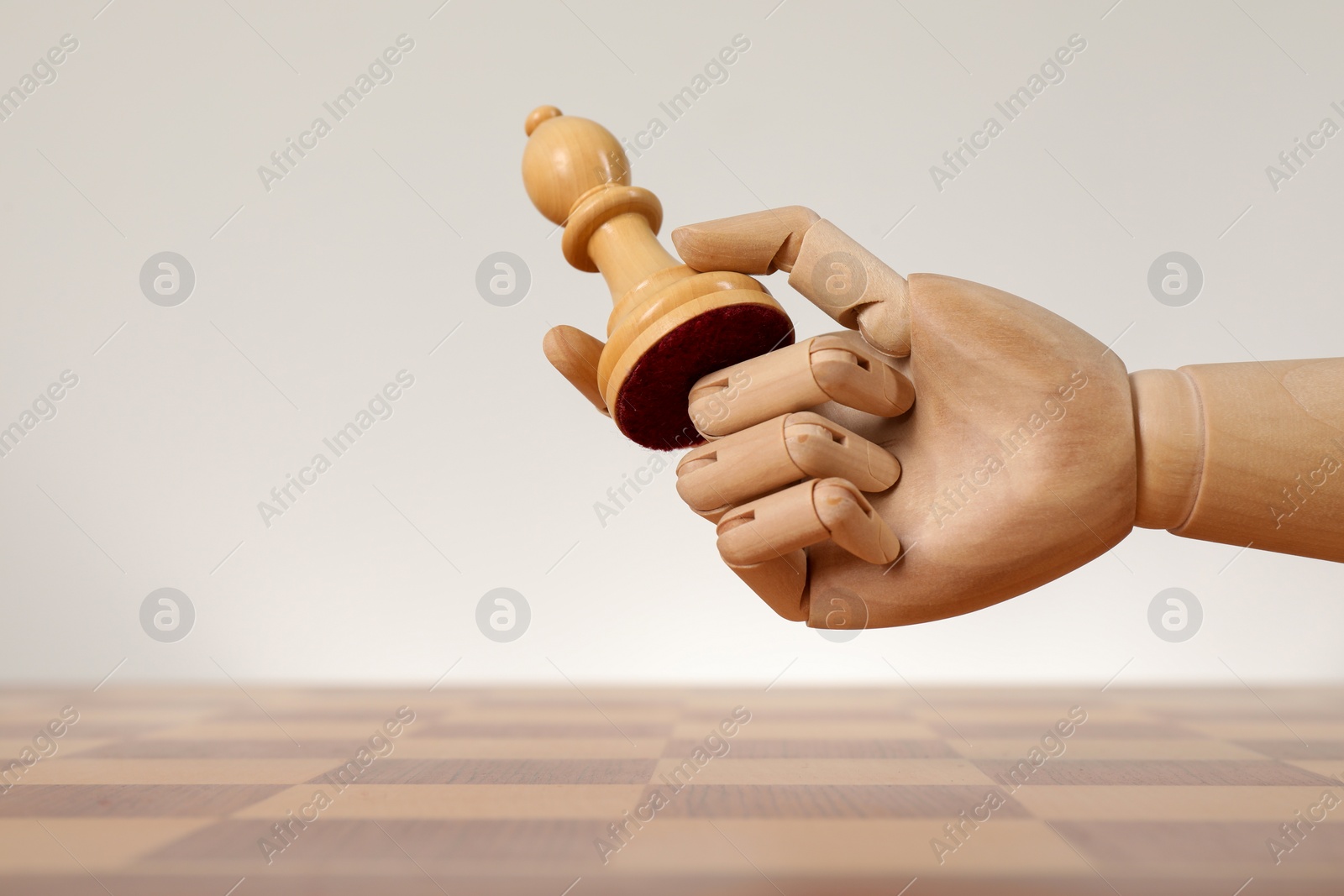 Photo of Robot with chess piece above board against light background, space for text. Wooden hand representing artificial intelligence